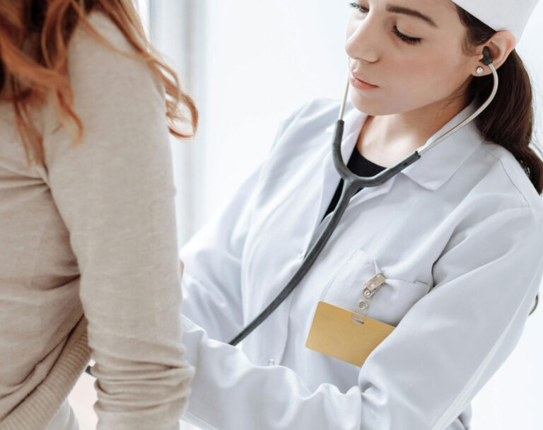 Eine Ärztin untersucht den Bauch einer Frau mit einem Stethoskop.