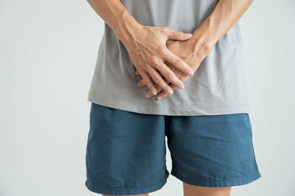 Young man in shorts and T-shirt, hands covering genitals.