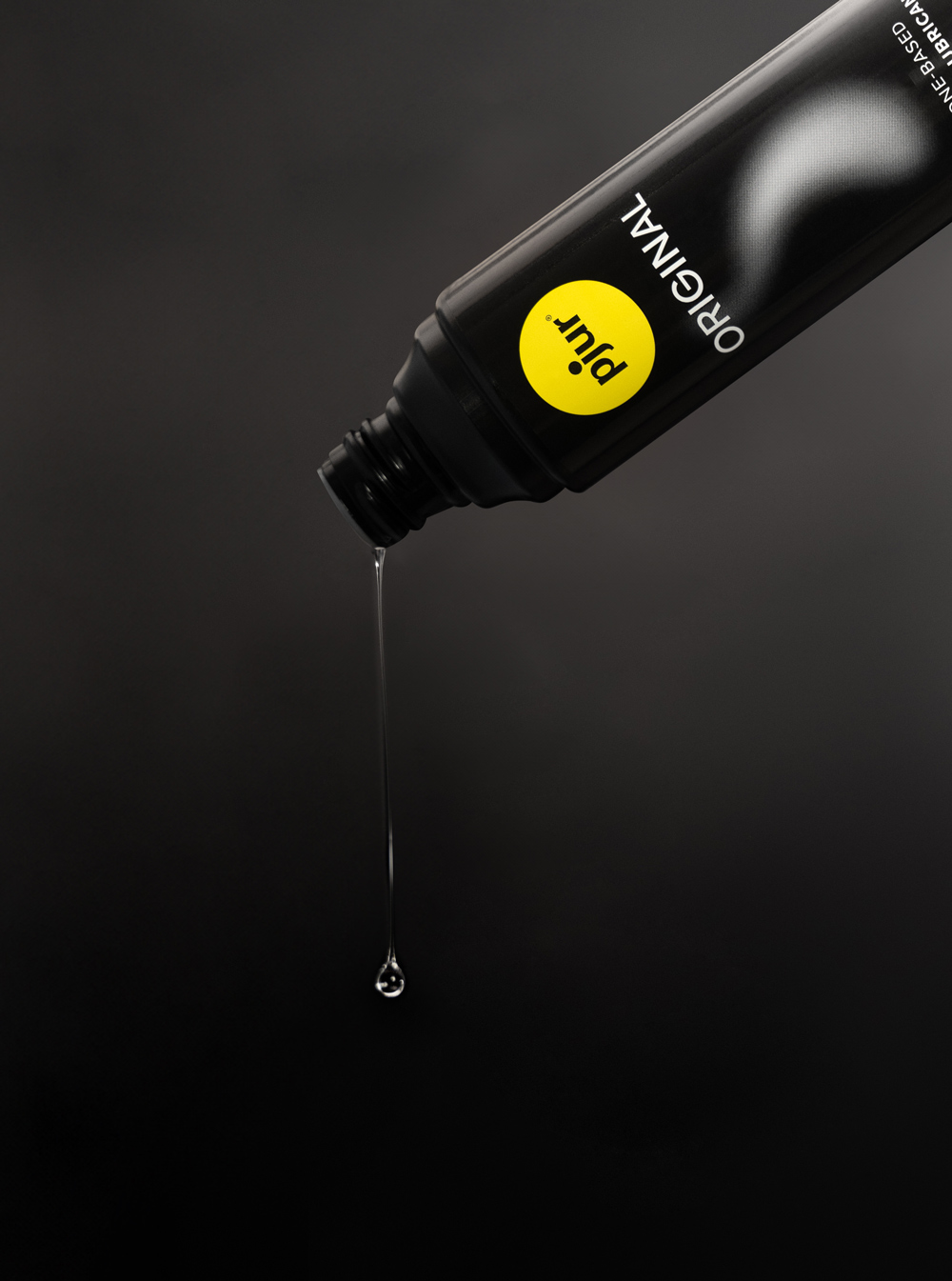 Schwarze Tube mit gelbem Logo, die Gleitgel enthält, mit einem Tropfen, der heraustropft.